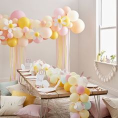 a table topped with lots of balloons in front of a window filled with pink, yellow and white balloons