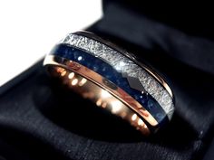 a wedding ring with blue and white diamonds in it on a black velvet box,