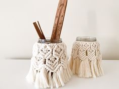 two mason jars with tassels are sitting on a white counter top, one has a wooden handle and the other has a pair of scissors in it