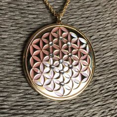 "Flower of Life in 24 carat gold on 925 silver, rose mother of pearl and crystals Sephiroth. Found in the most sacred places on Earth, its pattern evocates each form in nature as it is known. For the first time it appeared in the Temple of Osiris built in 1650 ac. Its shapes hidden the fruit of life and it presents a triangolar lattice form, with circle radii equal to their separation is called a seven overlapping circles grid. It contains six circles intersecting at a point, with a seventh circ Rose Gold Jewelry With Large Pendant As Gift, Pink Gold Pendant Necklace As A Gift, Pink Gold Flower Pendant Necklace As Gift, Rose Gold Pendant Locket Necklace, Rose Gold Medallion Necklace In Amulet Style, Pink Medallion Jewelry For Gifts, Pink Medallion Jewelry As A Gift, Gold Crystal Necklace With Pearl Pendant For Gift, Pink Medallion Necklace For Gifting