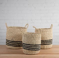 three black and white striped baskets sitting on top of a wooden table next to a brick wall