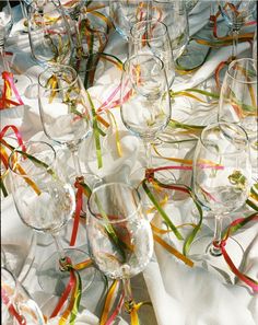 many wine glasses are lined up on a white table cloth with ribbons in the middle