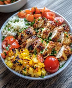 a white bowl filled with chicken, rice and veggies next to a bowl of tomatoes