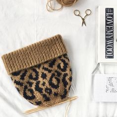 a pair of scissors, yarn and knitting needles on top of a white sheet with an animal print purse