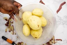 a person is holding a plastic bowl full of potatoes on a marble counter top with other ingredients in the background