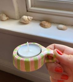 a person holding a small candle in front of a window sill with seashells on the windowsill