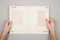 two hands are holding an open book with writing on the pages and in red lettering