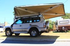 an suv with a tent attached to it parked on the side of the road in front of a trailer