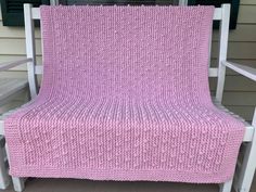 a pink crocheted blanket sitting on top of a white rocking chair in front of a house