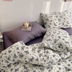 an unmade bed with purple sheets and pillows on it, next to a night stand