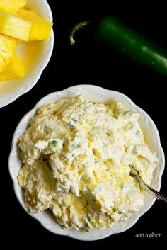 two bowls filled with mashed potatoes next to some green peppers and a pickle