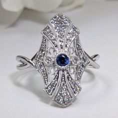 Art Deco Diamond & Blue Sapphire Fashion Ring, Filigree Design 14k White Gold DIAMOND DETAILS: Shape:  Round Cut Diamonds Number of Stones: 44 Carats:  0.20 ct. Clarity: VS-SI - Eye Clean  Color: H-I GEM STONES: Shape:  Round Cut Blue Sapphire Number of stones: 1 Approx. 0.05 ct. Clarity: Eye Clean  Color: Medium Blue SETTING: Material: 14k White Gold (Available Also in 14K Yellow Gold or 14K Pink Gold - No Extra Charge) Ring size 7 (custom made in other sizes) Comes packaged In Pop up gift box Art Deco Blue Diamond Ring With Accents, Blue Art Deco Diamond Ring With Accents, Fine Jewelry Sapphire Ring For Wedding With Intricate Design, Sapphire Ring With Intricate Design For Wedding, Wedding Sapphire Ring With Intricate Design, Fine Jewelry With Accent Stones For Collectors, Classic Marquise Jewelry With Intricate Design, Formal Marquise Jewelry With Intricate Design, Blue Art Deco Diamond Ring With Diamond Cut