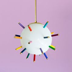 a multicolored light fixture hanging from a purple wall with colored pencils all over it