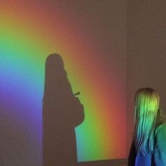 a woman standing in front of a wall with a rainbow shadow on the wall behind her