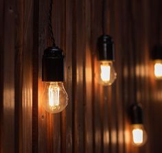 some light bulbs are hanging on the wall with wood paneling in the back ground