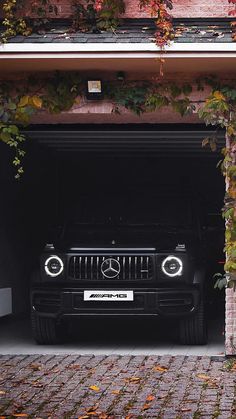 a black car parked in a garage with ivy growing on the wall and door open