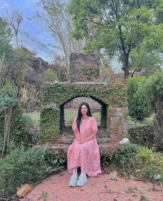 a woman in a pink dress sitting on a brick patio