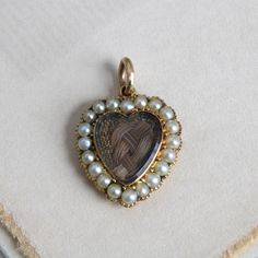 "Circa 1840 an antique Victorian heart-shaped locket charm crafted in 14k yellow gold featuring a beveled-glass covered compartment holding a beautifully woven love-knot of chestnut brown hair. With the pearl surround (likely natural pearls but not tested) set in cut-down collets and the back extravagantly chased in a lush acanthus leaf pattern and \"B. Hunter\" engraved on a ribbon banner, it's a poignant and rare example of early Victorian mourning jewelry. Measuring approximately 7/8\" north Victorian Jewelry With Heart Charm For Anniversary, Victorian Locket Jewelry For Valentine's Day, Victorian Locket For Valentine's Day, Victorian Yellow Gold Jewelry For Valentine's Day, Victorian Medallion Jewelry For Valentine's Day, Victorian 14k Gold Jewelry For Valentine's Day, Victorian Medallion Jewelry With Heart Charm, Victorian 14k Gold Heart-shaped Jewelry, Victorian 14k Gold Heart Shaped Jewelry