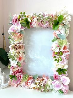 a white table topped with a pink and green flower frame next to a potted plant