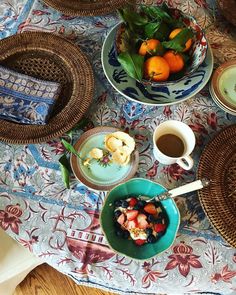 a table topped with plates and bowls filled with fruit next to a cup of coffee