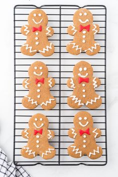 four ginger cookies with red bow ties on a cooling rack next to a plaid napkin