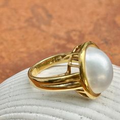 New, but old pieces, never worn, recently acquired from a premier jeweler located in Minneapolis, MN for many years- a rare opportunity! 18KT yellow Ggld genuine, bezel-set, white, oval, mabe pearl ring. Size 6.75 Sizable by us for a fee or your local jeweler Weight: 10.3 grams Band width: 3mm in back Pearl measures: 15mm x 11mm oval mabe pearl Stamped 18k By Honora Timeless Oval Rings With High Luster, Elegant White Domed Rings, High Luster Oval Yellow Gold Rings, High Luster Yellow Gold Oval Rings, Timeless Gold Dome Ring With Cabochon, Classic Gold Pearl Ring With Polished Finish, Heirloom Pearl Ring In Yellow Gold With High Luster, Elegant Domed Jewelry With Bezel Setting, Gold Dome Ring With Cabochon For Formal Events