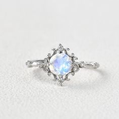 a white ring with an opal center surrounded by small diamonds on a white surface