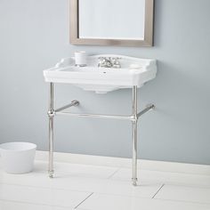 a bathroom sink sitting under a mirror next to a trash can and cup on the floor