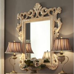 a mirror sitting on top of a dresser next to two lamps and a lamp shade