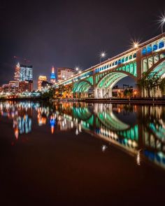 a bridge that is over some water with lights on it and buildings in the background