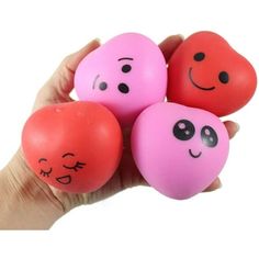 hand holding four plastic balls with faces painted on them in the shape of hearts and eyes