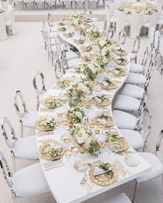 a long table is set with white chairs and gold place settings for an elegant dinner