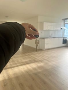 a hand holding a house key in an empty room with white cabinets and wood floors