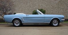 a light blue mustang parked in front of a brick wall