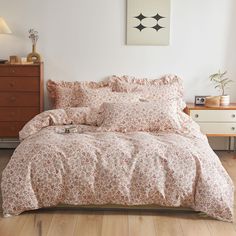 a bed with pink and white flowers on it in a room next to a dresser