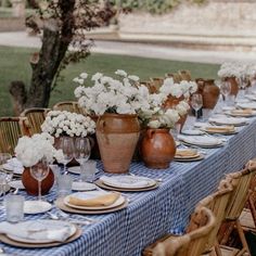 a table set with plates and vases filled with white flowers on top of a blue checkered table cloth