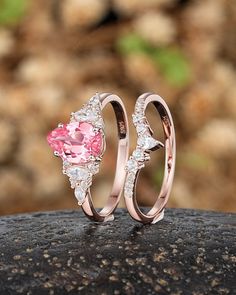 two wedding rings with pink and white diamonds on top of a rock in front of some rocks