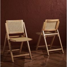 two wooden chairs sitting next to each other on top of a hard wood floor in front of a red wall