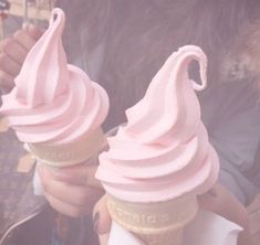 two ice cream cones with pink icing on top are being held by someone's hands