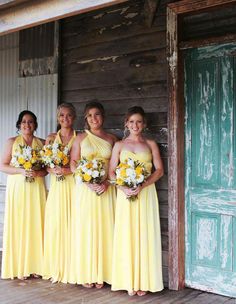 four bridesmaids in yellow dresses posing for a photo outside an old wooden building