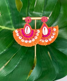 Introducing our "Finding Shells" Earrings in Orange/Fuchsia, a delightful addition to your summer accessory collection. These earrings feature small sea shells beautifully adorned with vibrant orange and fuchsia beads, creating a charming and beachy look. Crafted in a teardrop tassel style, they offer a playful and elegant aesthetic. With a secure post closure and measuring 2.75 inches, they are both stylish and comfortable to wear. Add a touch of seaside charm to your outfit with the "Finding Shells" Earrings in Orange/Fuchsia, perfect for embracing the spirit of summer! Multicolor Summer Earrings, Coral Bohemian Beach Jewelry, Bohemian Coral Jewelry For Beach, Bohemian Coral Jewelry For The Beach, Handmade Shell Earrings For Summer, Handmade Beachy Earrings For Summer, Summer Beach Dangle Earrings, Handmade Pink Beaded Earrings For Beach, Handmade Beaded Earrings For Beach