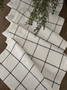 four white and black checkered napkins sitting on top of a wooden table next to a potted plant