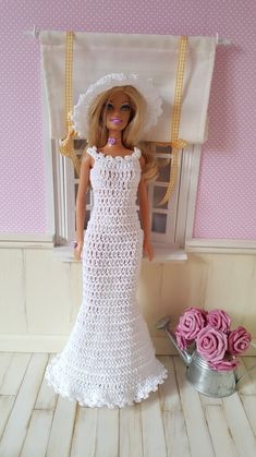 a doll in a white dress and hat next to pink roses