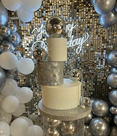 a three tiered cake sitting on top of a table surrounded by balloons and confetti