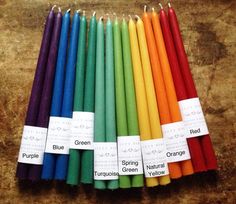 many different colored candles are lined up on a table with labels that read purple, green, orange, and red