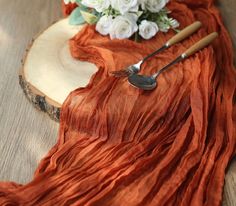 an orange table runner with flowers and utensils sitting on top of it next to a wooden slice