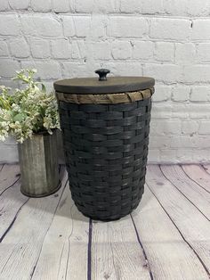 a black basket next to a metal container with flowers in it on a wooden floor