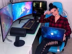 a woman sitting in front of a computer desk with a laptop and monitor on it