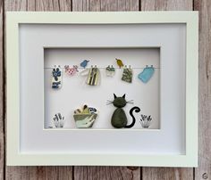 a white frame with a cat and clothes pins in it on a wooden surface next to a wall