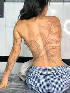 a woman sitting on top of a bed with tattoos on her back and arms behind her